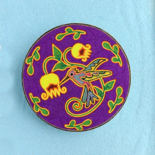 Handmade Huichol yarn painting showing a colorful hummingbird drinking from yellow flowers, crafted with yarn and beeswax on a 20cm round wooden base. Front image