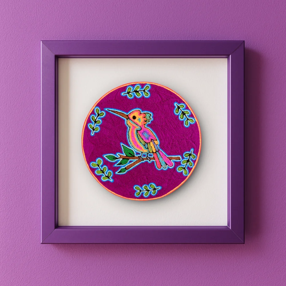 Handmade Huichol yarn painting showing a colorful hummingbird on a branch with green leaves, crafted with yarn and beeswax on a 20cm round wooden base. Framed IMage