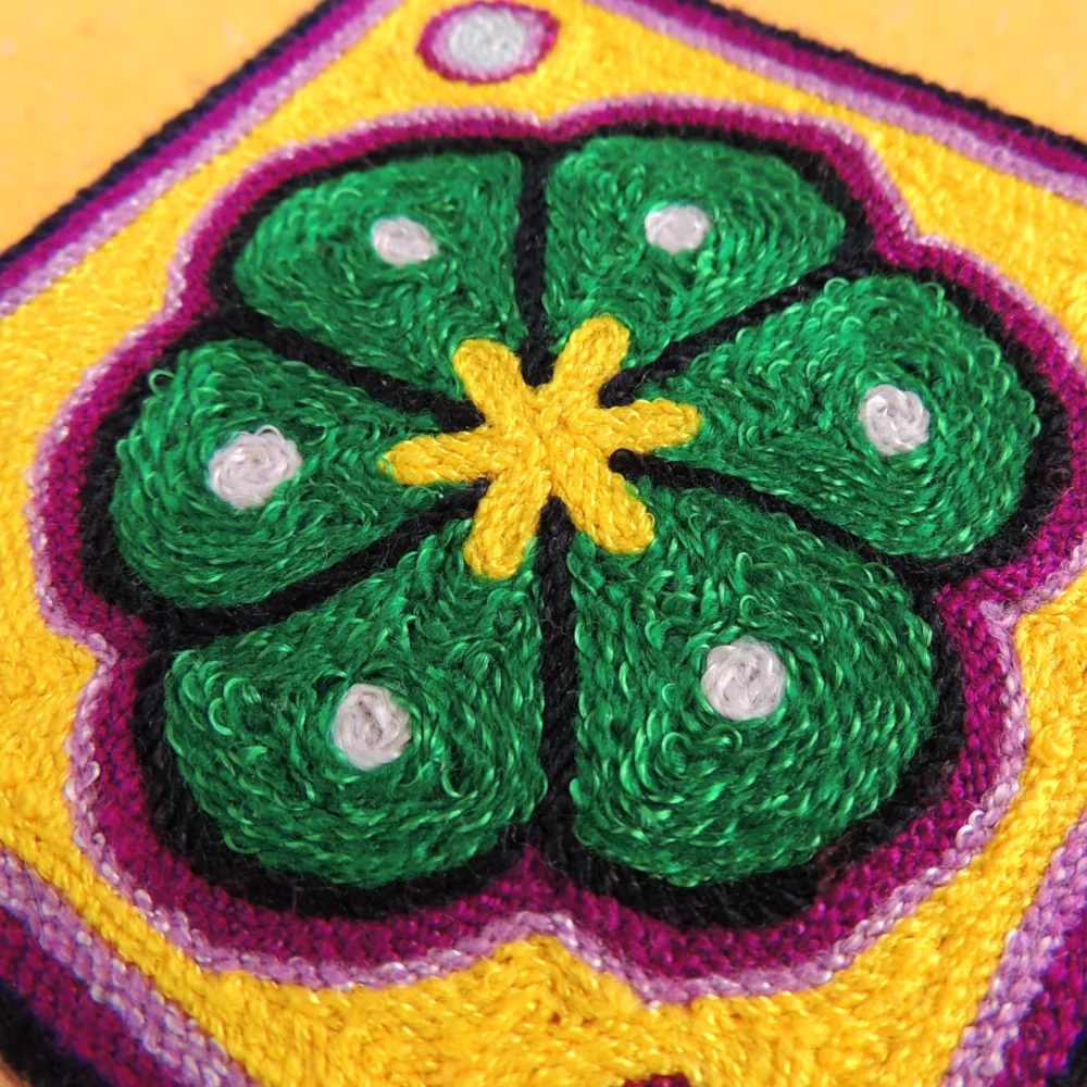 Close-up of a Huichol yarn painting highlighting textured yarn lines forming a green peyote flower.