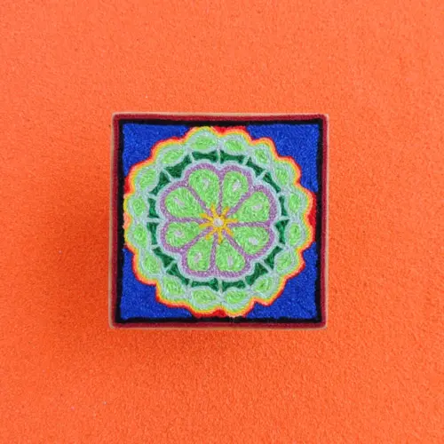 Front view of Huichol yarn painting with layered green peyote on blue base.