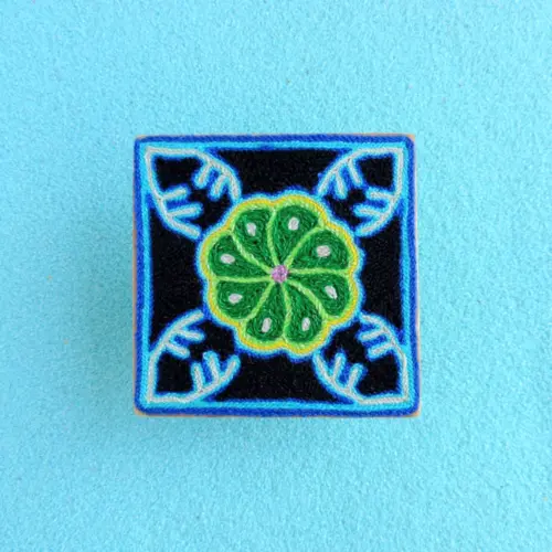 Front view of Huichol yarn painting with green peyote and blue corners.